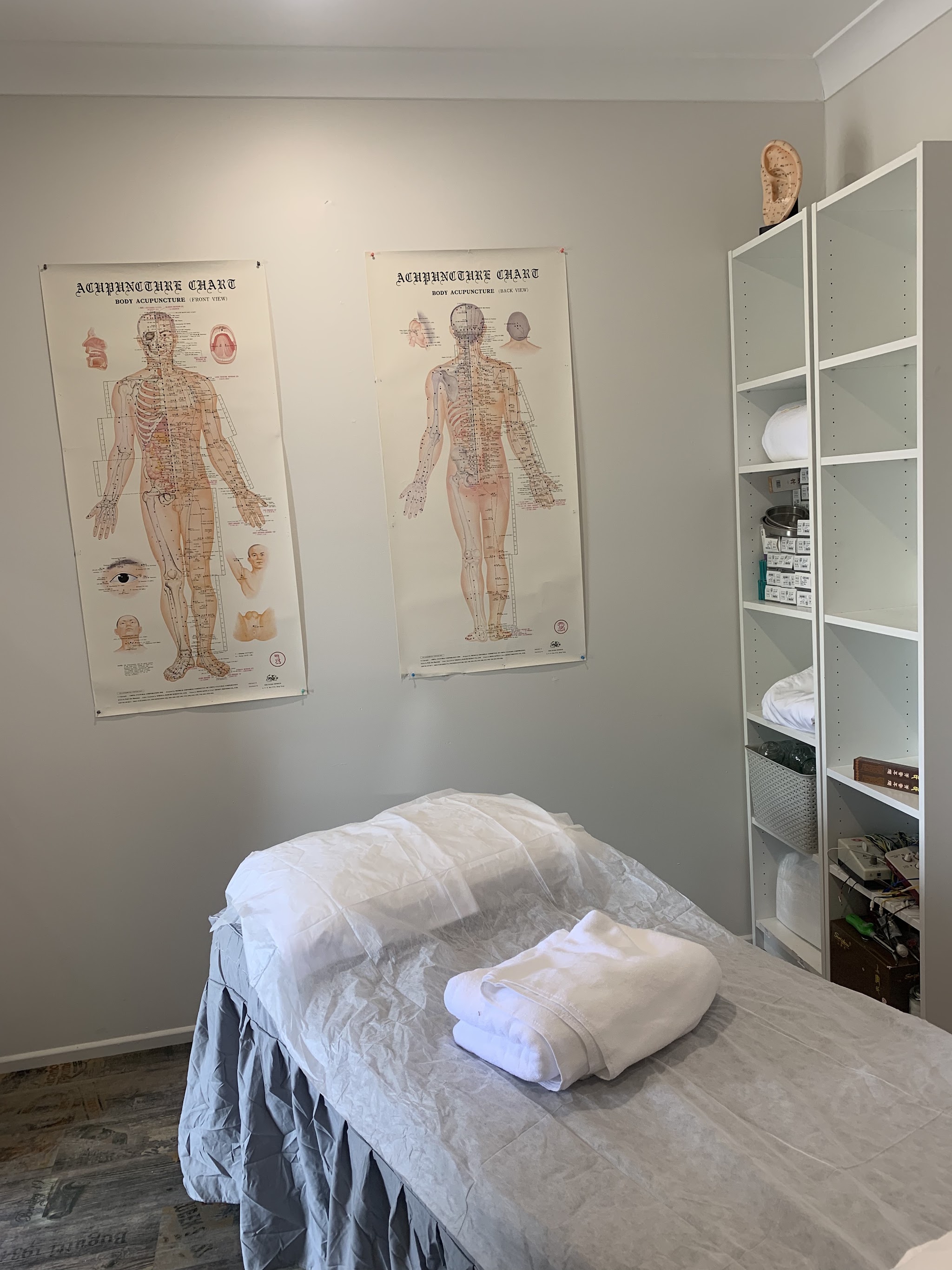 A treatment room made up with fresh white linen, acupuncture wall charts behind